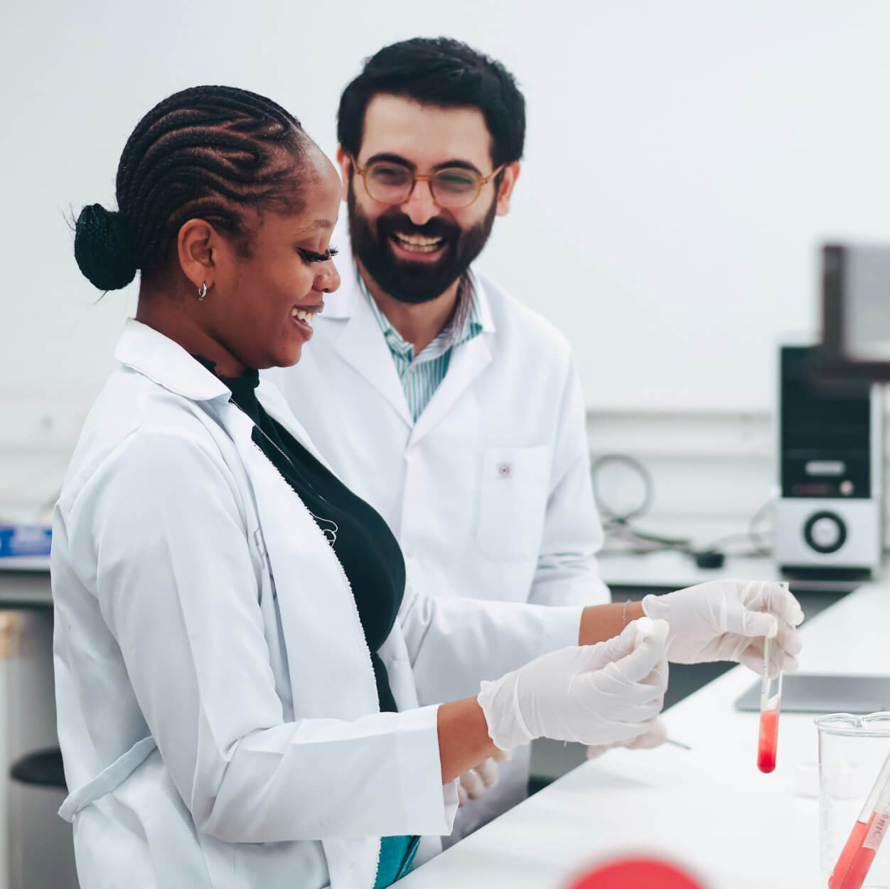 Deux scientifiques en blouse blanche collaborent dans un laboratoire, l'une tenant une éprouvette contenant un échantillon rouge.