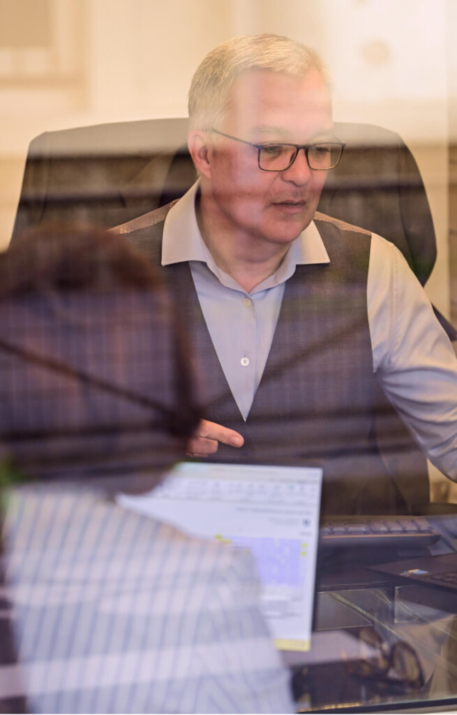 Lionel GUÉRIN, consultant en recrutement Learn2Fly RH, reçoit un candidat à son bureau, vu à travers une paroi vitrée lors d'un entretien professionnel.