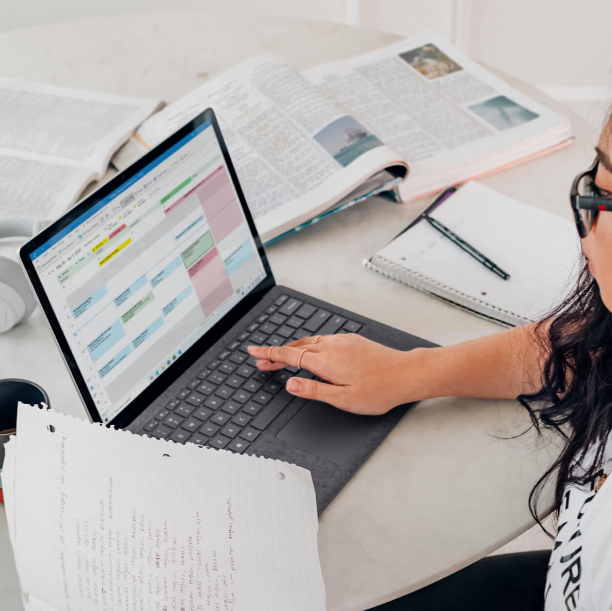 Une professionnelle consulte un agenda numérique sur son ordinateur portable entourée de livres et de notes de travail.