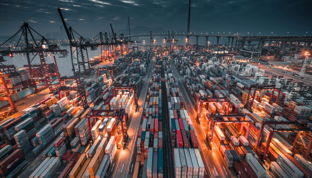 Vue aérienne nocturne d'un terminal portuaire avec des milliers de conteneurs maritimes empilés et des grues de chargement.
